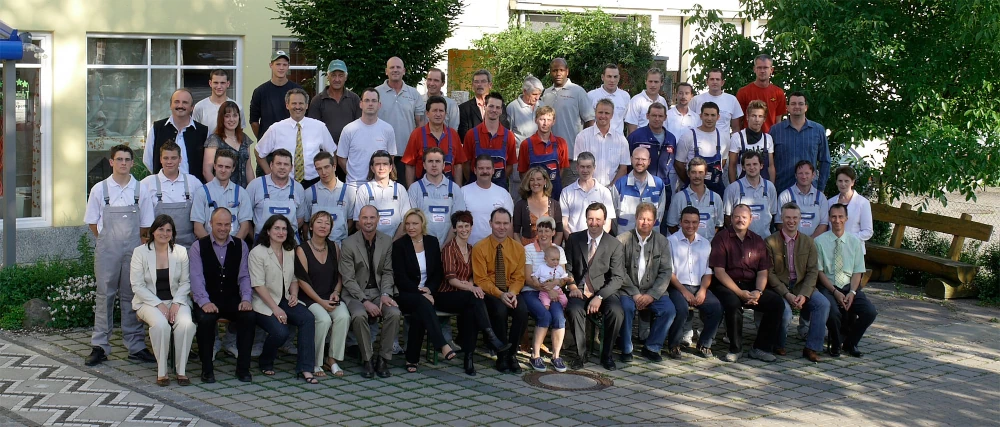 Gruppenfoto von Mitarbeitern in Arbeitskleidung vor Firmengebäude im Freien